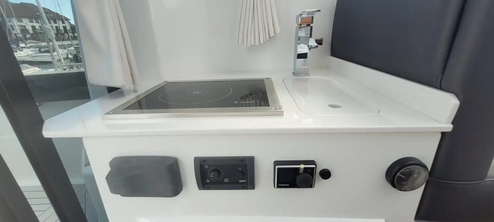 Modern boat kitchenette featuring an induction cooktop, sink, and control panel with visible text and nautical appliances.